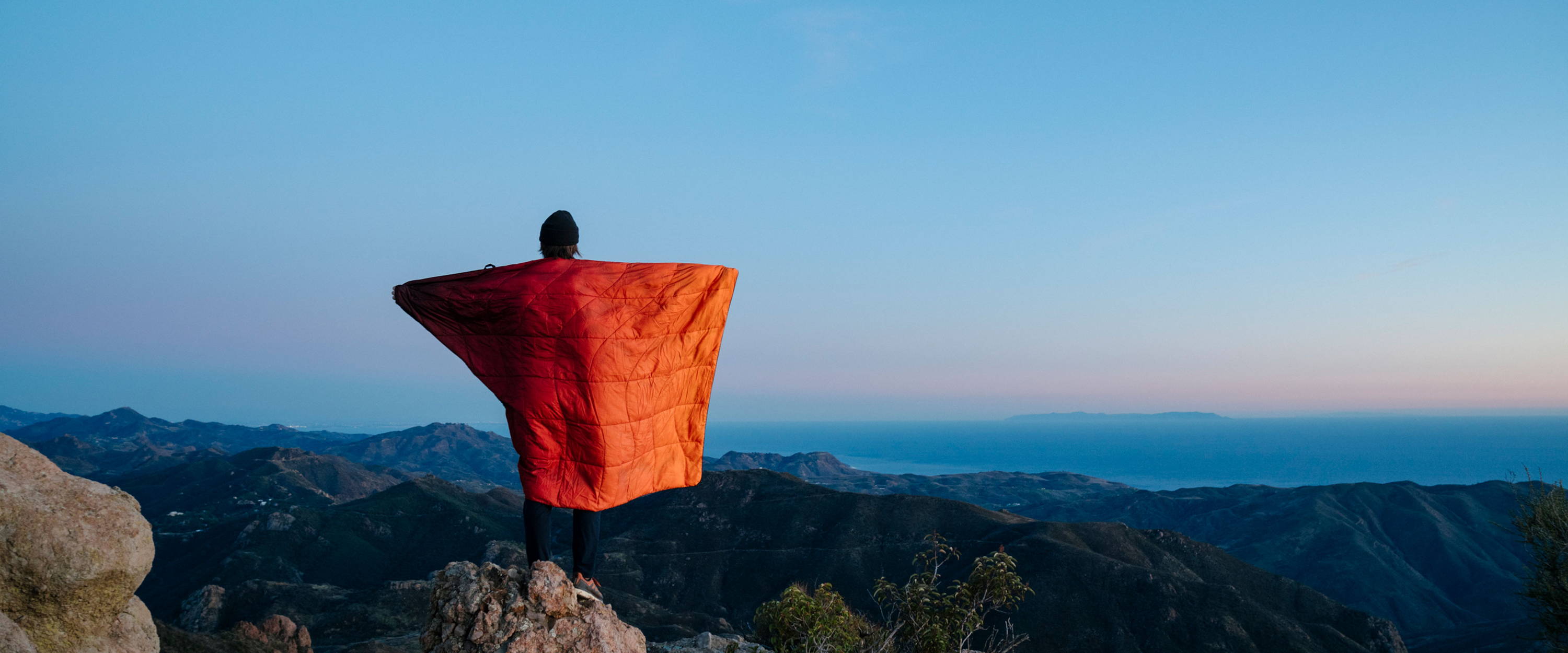 Man standing at vista over looking mountains in a Rumpl blanket