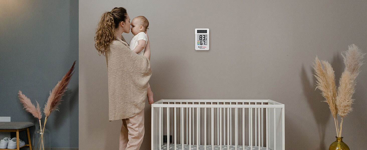 Mother holding baby near a crib in a modern nursery.