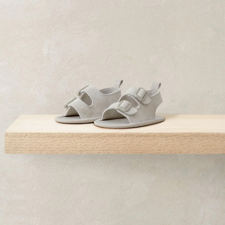 Gray children's sandals displayed on a wooden shelf.