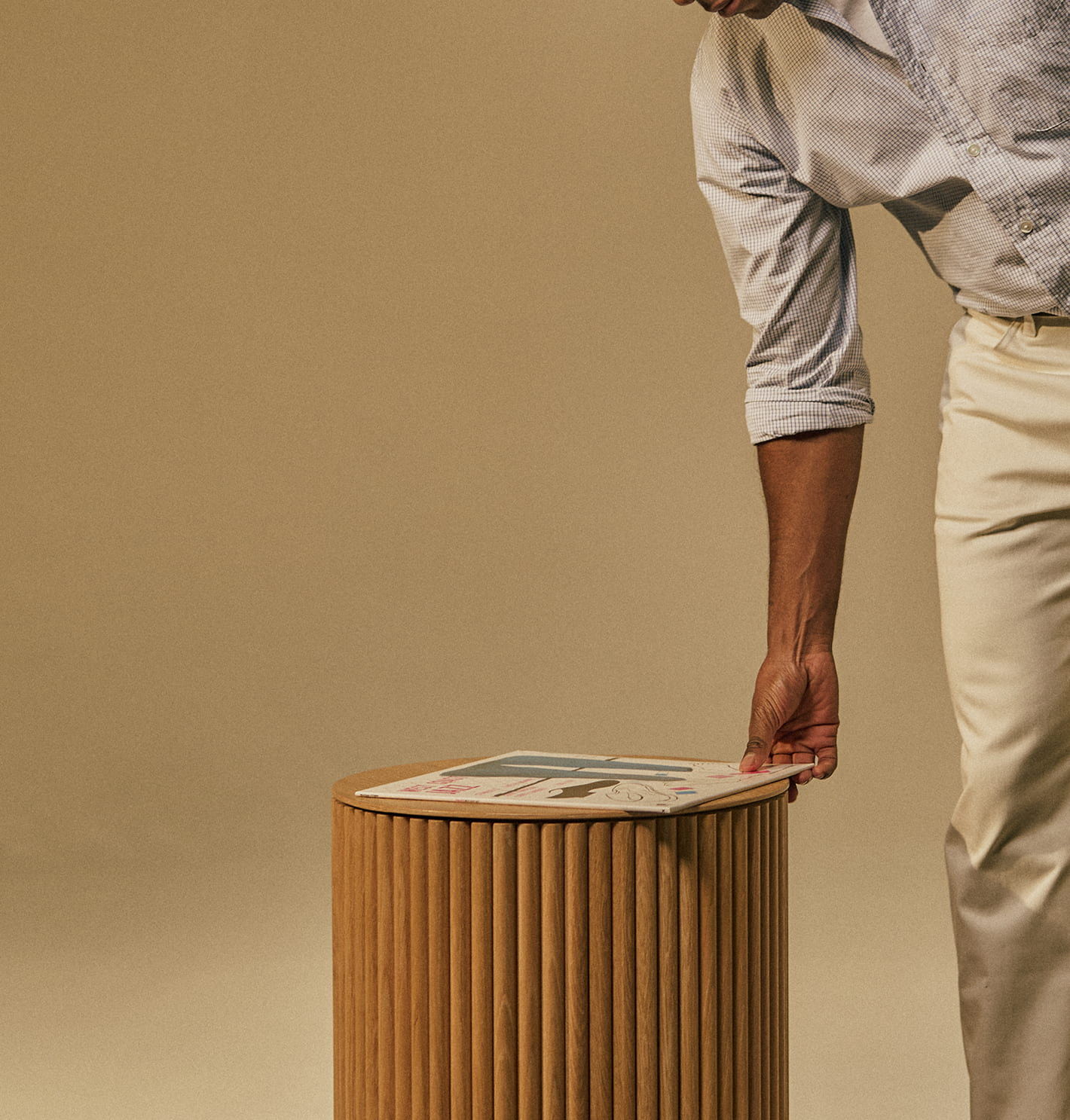 Person placing a magazine on a wooden, ribbed side table.