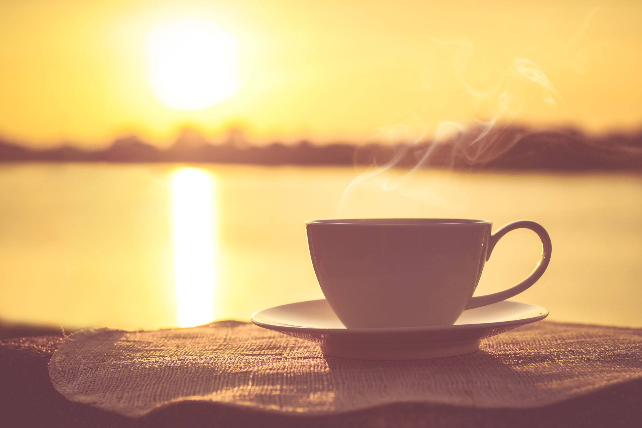 A small cup of Perk Energy sitting on a plate outside with a sunrise over a lake in the background