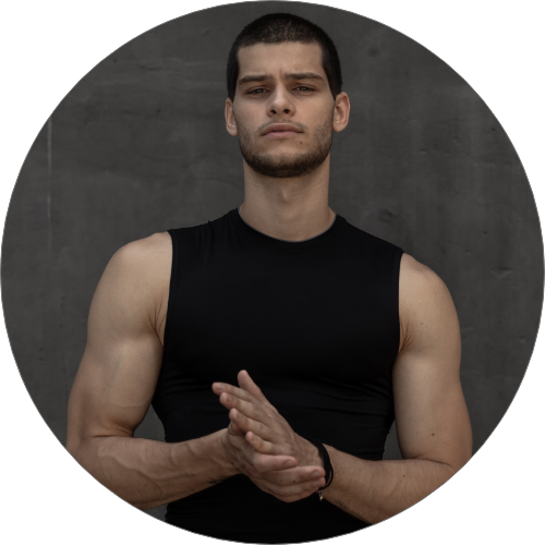 Young man in a sleeveless black shirt, posing confidently against a gray background.
