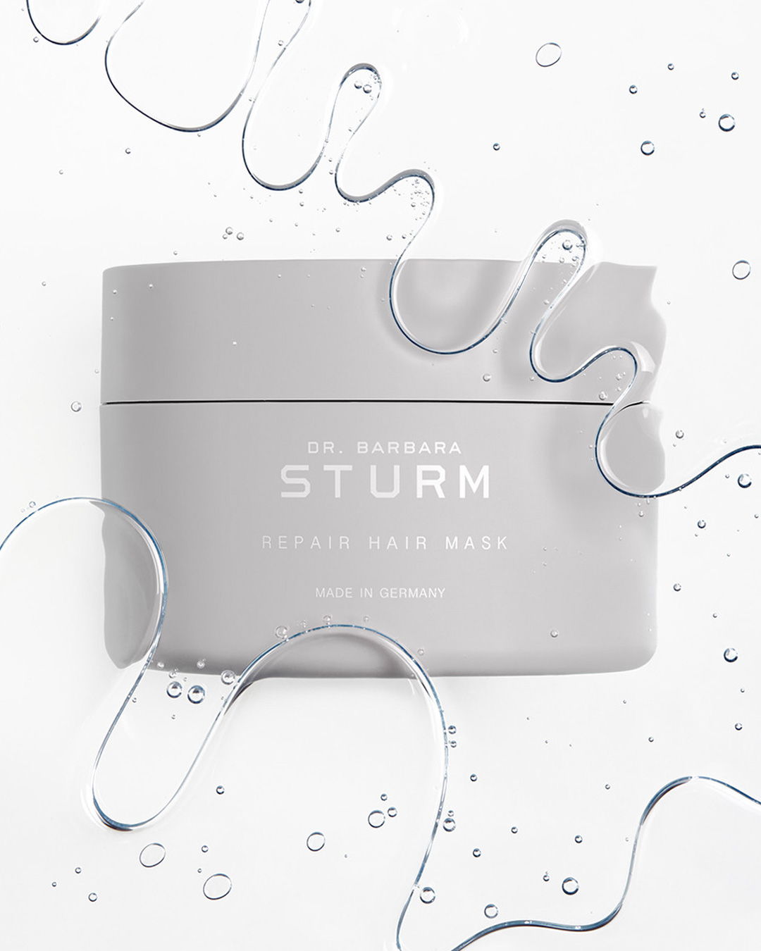 Gray skincare cream jar surrounded by water droplets and fluid shapes.