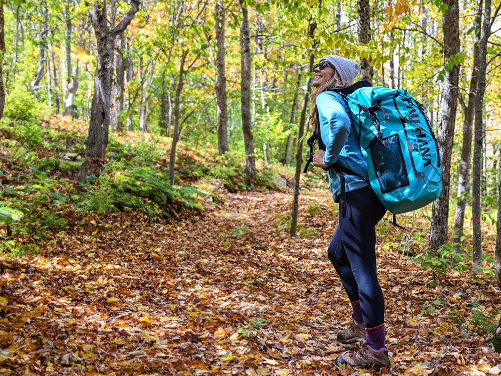 A woman walking with an inflatable paddleboard in a backpack through the woods.
