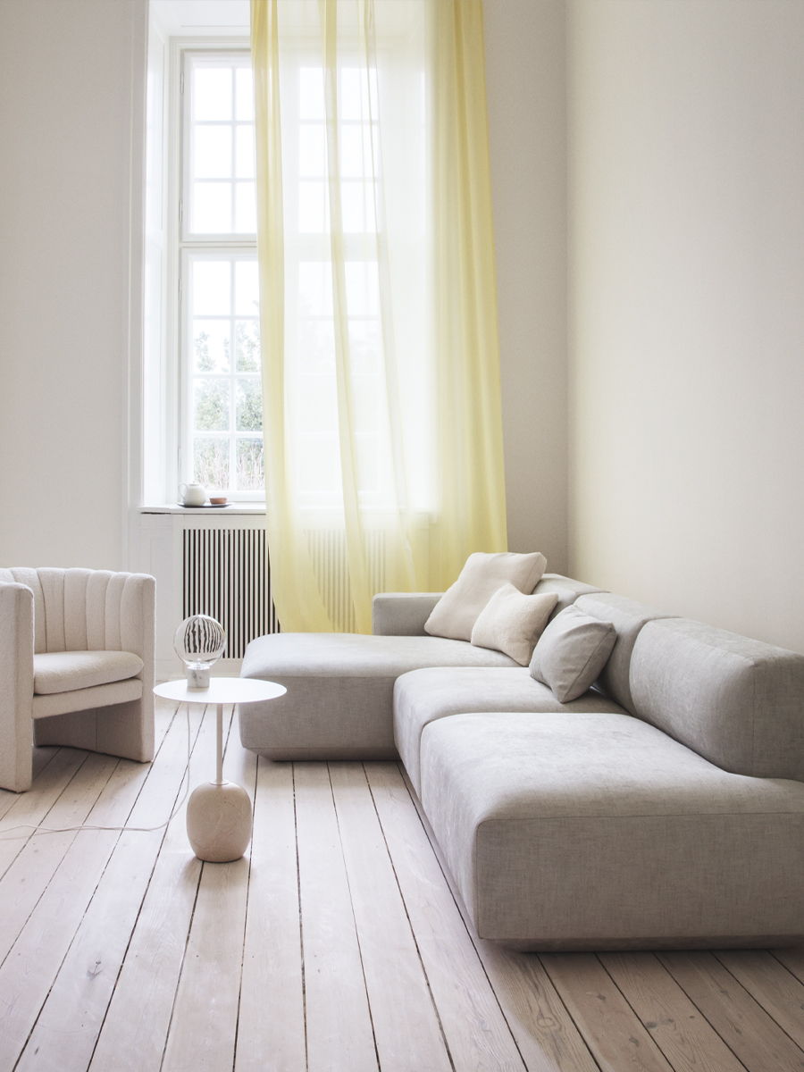 A modern living room with a light Develius sofa by &Tradition, armchair, and yellow curtains.