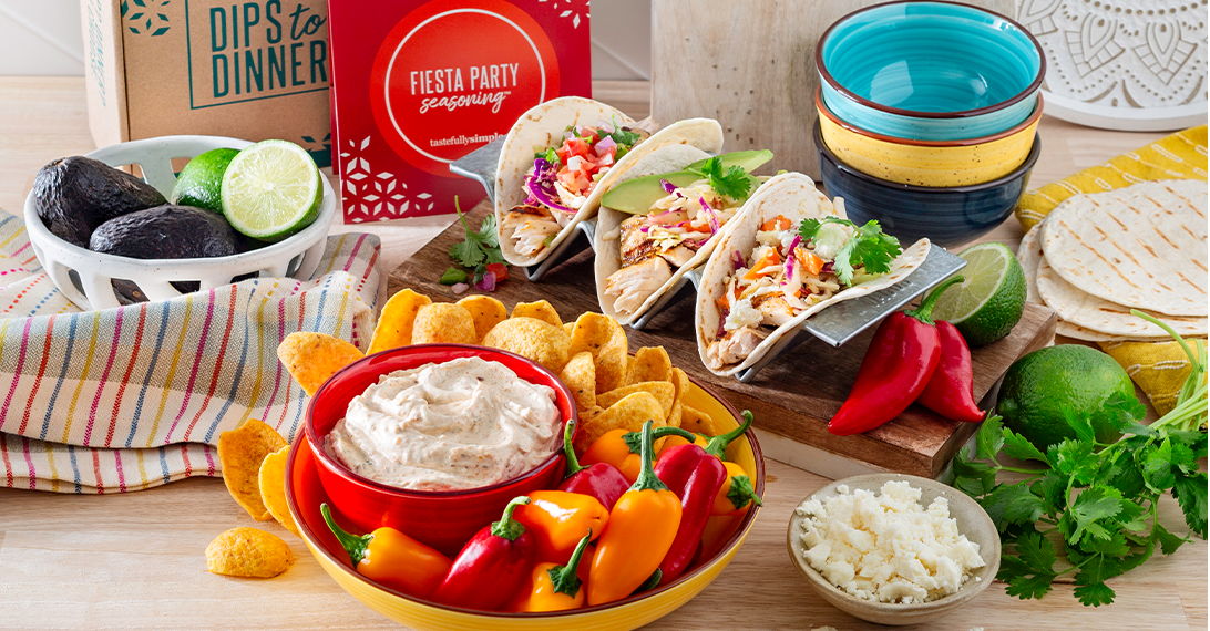 Dips to Dinner gift box and Fiesta Party Seasoning™ displayed with tacos, creamy dip, tortilla chips, peppers, avocados, and limes. View dips to dinner product page.