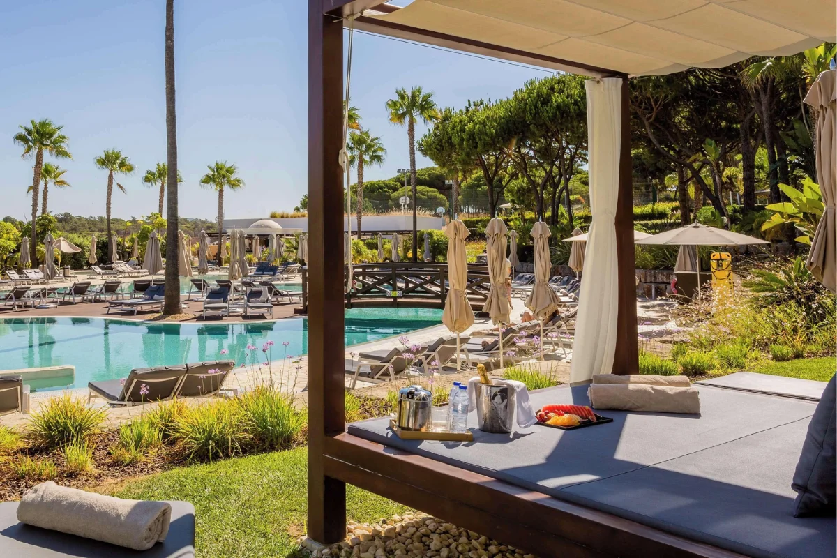 Hotel pool cabana with cushioned outdoor lounge seating overlooking a landscaped hotel pool deck