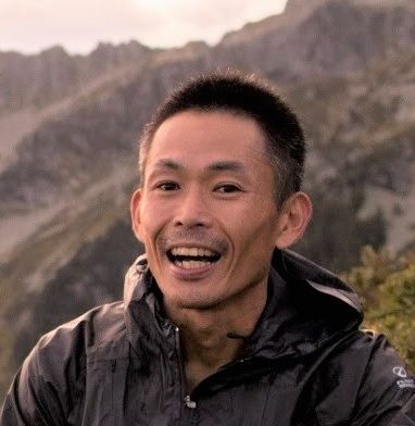 Smiling man in a black jacket, mountains in the background.
