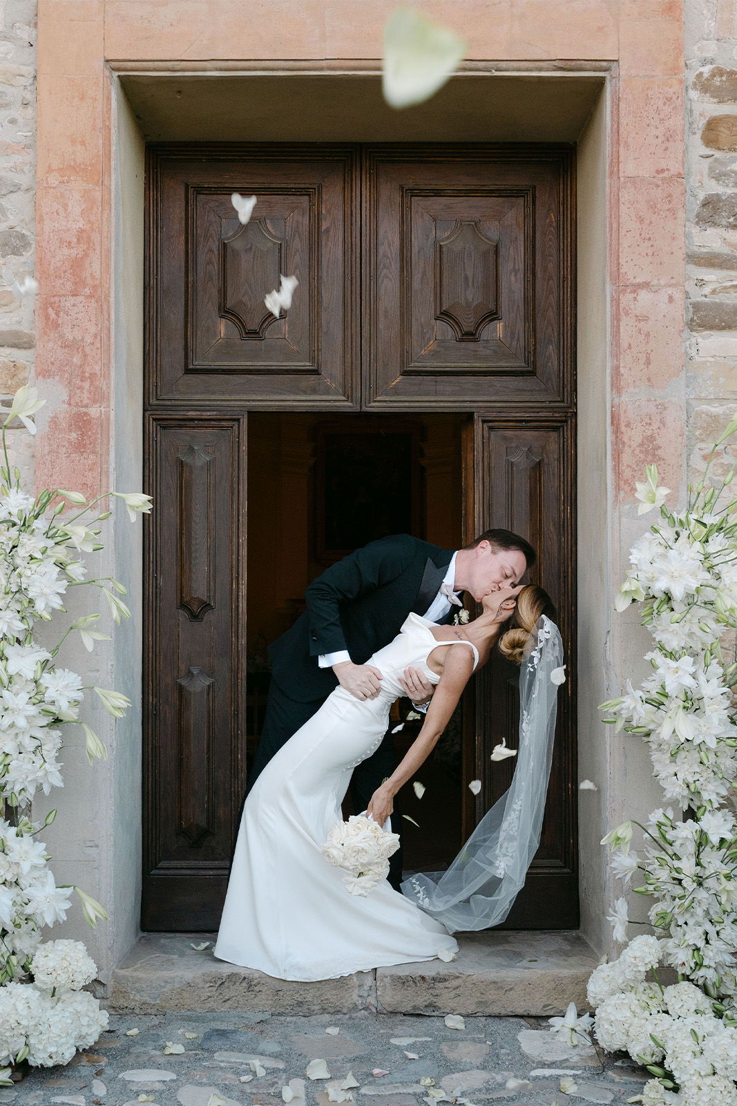 Bride and groom sharing a kiss in a floral-decorated doorway.