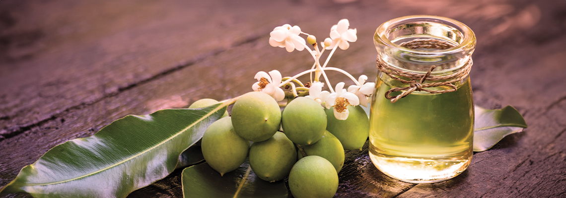 A bottle of oil with green olives and leaves on a wooden surface.