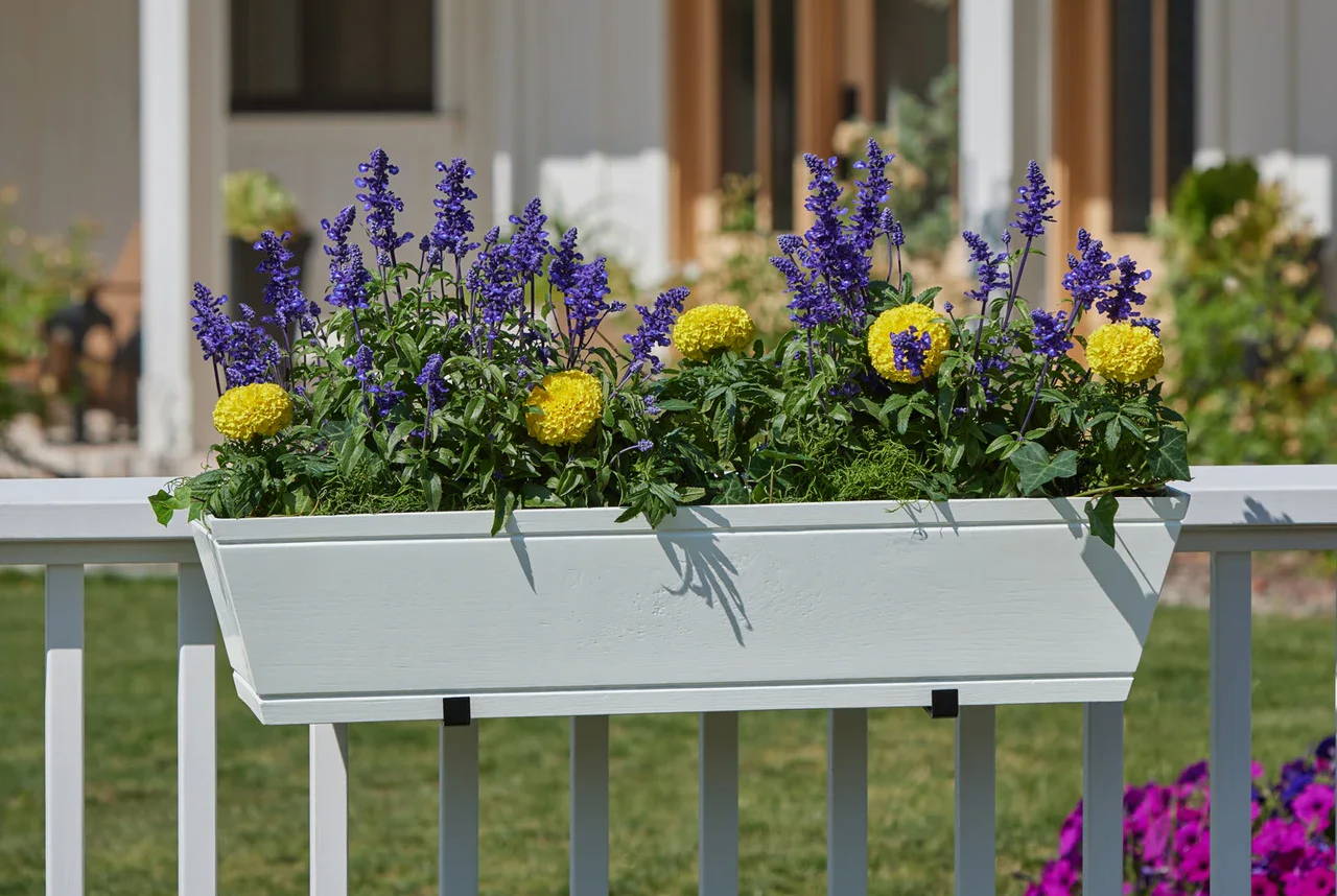 A Modern Farmhouse flower box with purple and yellow flowers on a white railing.