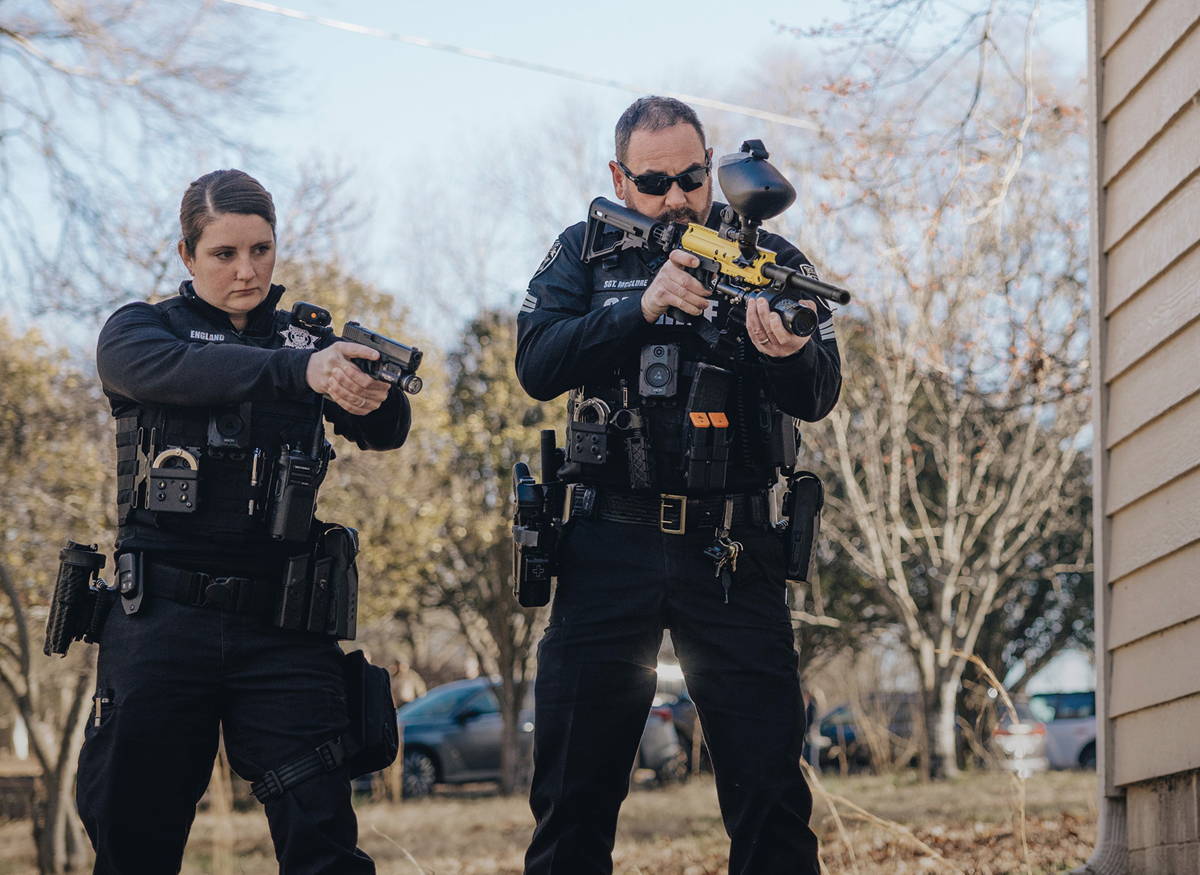 Two police officers aiming firearms outside a building.