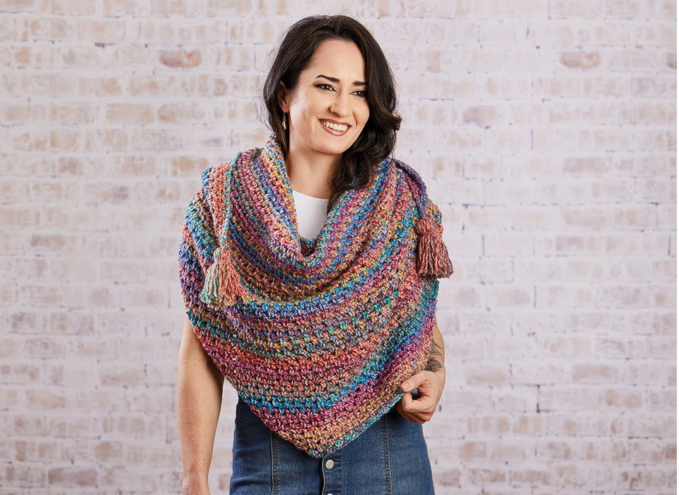 Woman wearing a colorful shawl, smiling against a brick wall backdrop.
