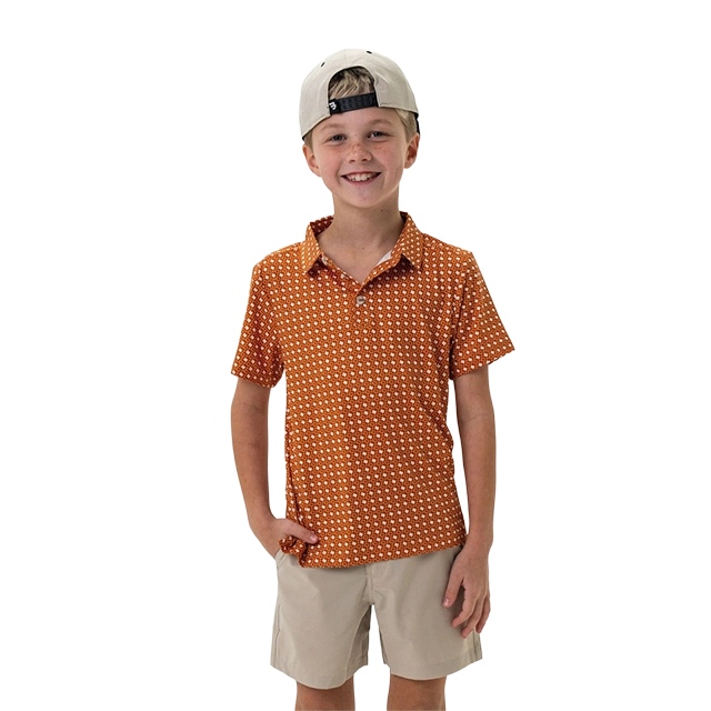 Smiling boy in orange patterned shirt and cap, standing with hands on hips.