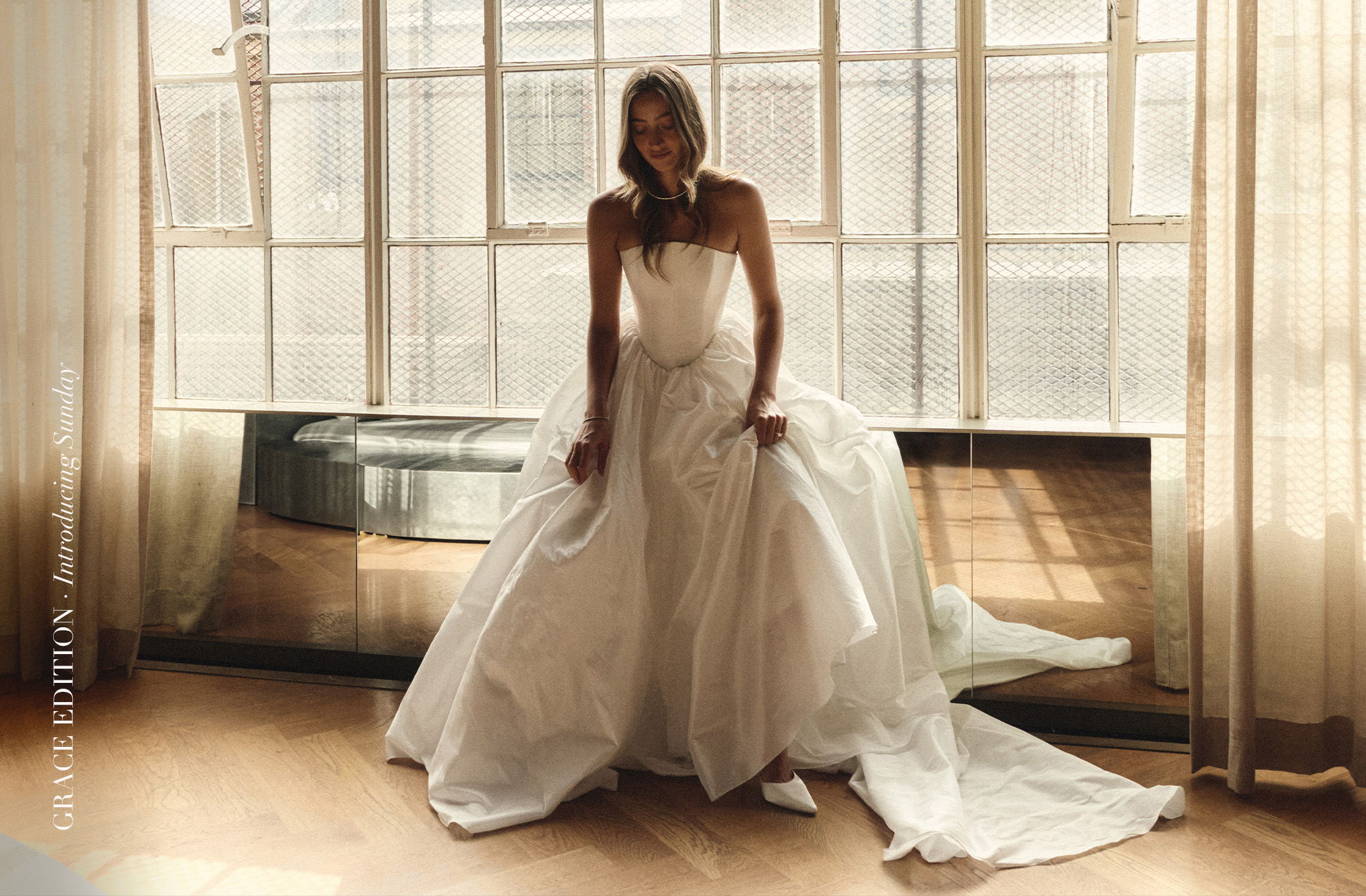 Woman in a white gown sitting near large windows.