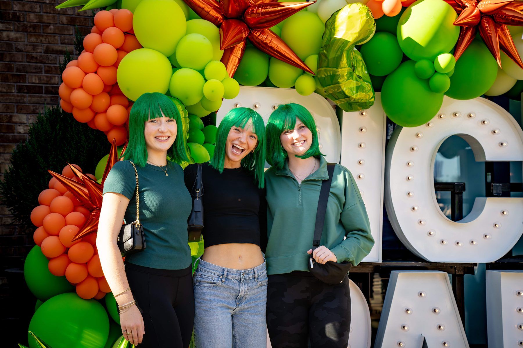 Three friends in matching green wigs posing at the PICKLE PARTY marquee letters and balloon installation at The Big Dill Arlington Texas 2025.