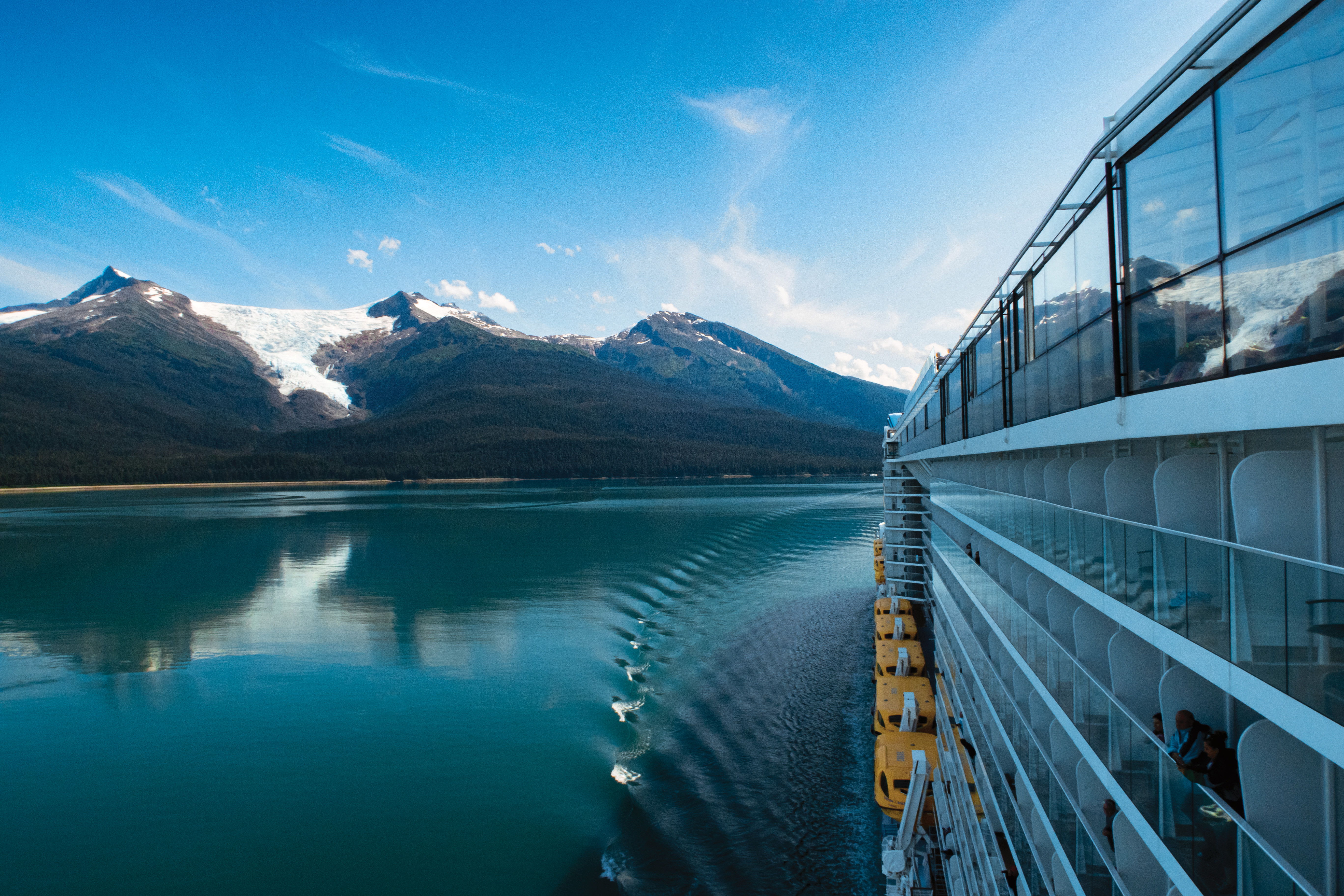Cruise ship beside a calm lake with mountains in the background.