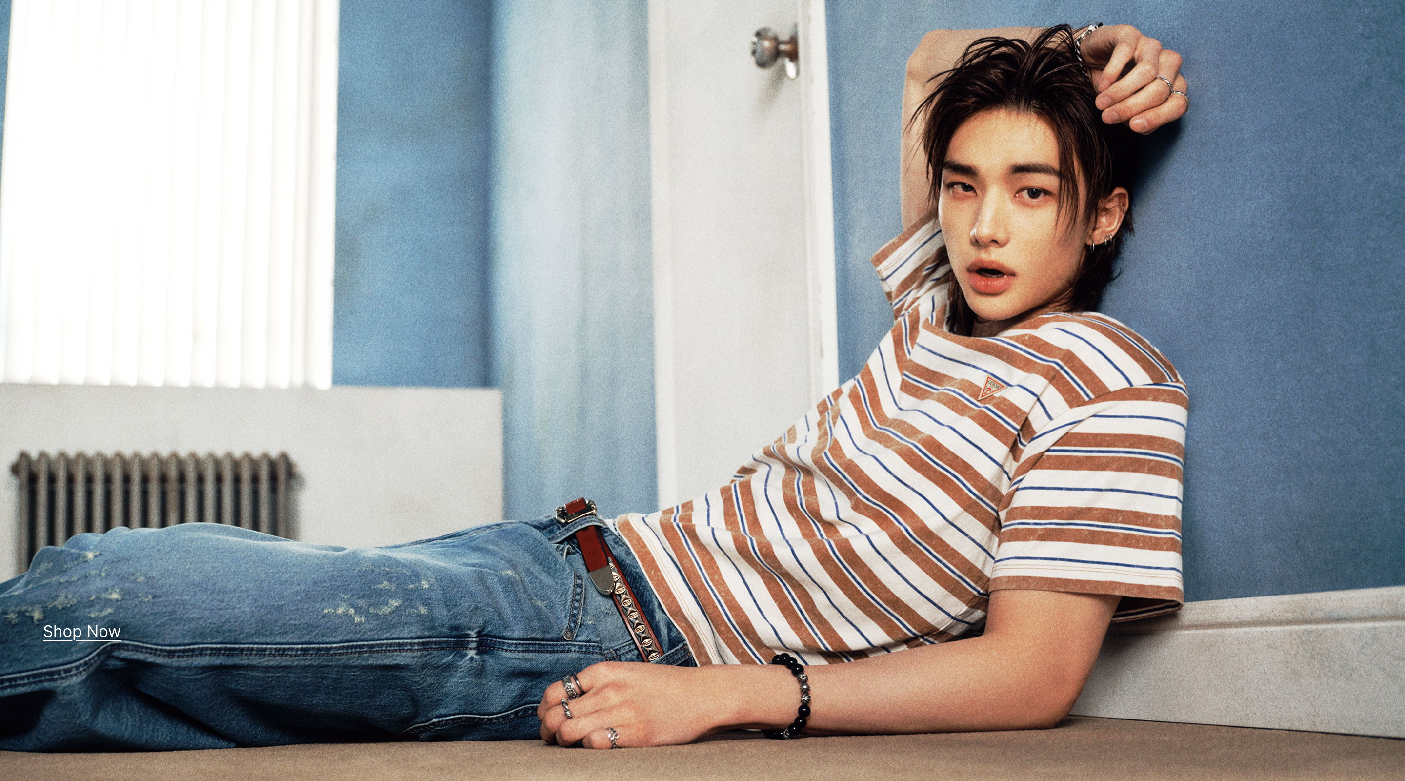 Hyunjin lounging against a wall, wearing a striped shirt and jeans.