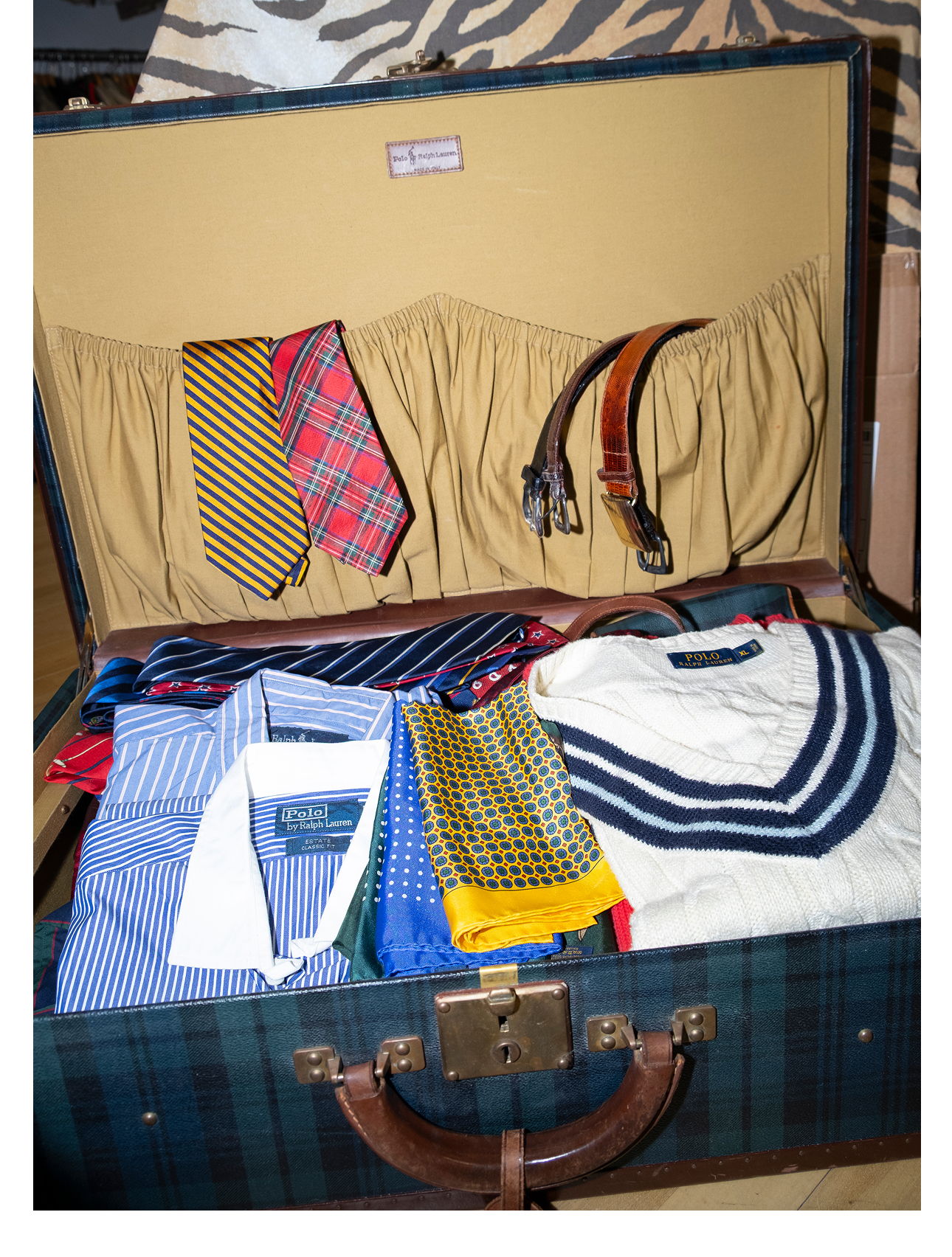 A suitcase filled with neatly arranged shirts, ties, and belts.
