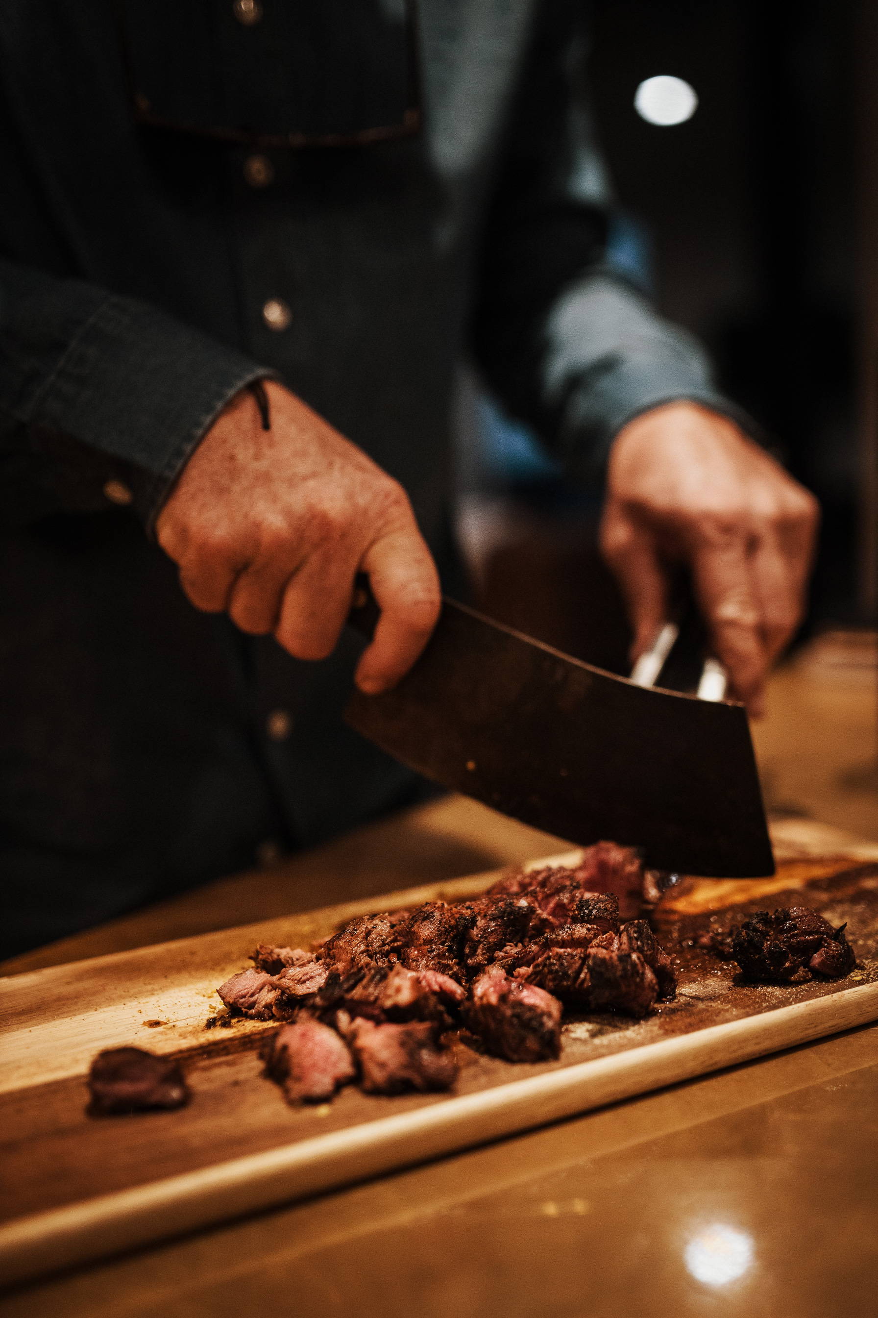 A man's hands cutting meat on a wooden cutting board.