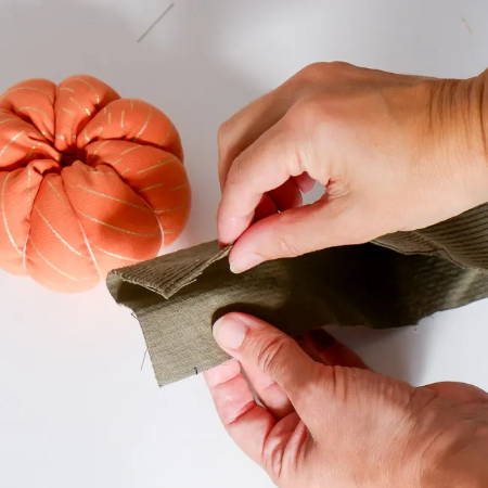 Hands folding a green fabric strip in half for the stem of the pumpkin