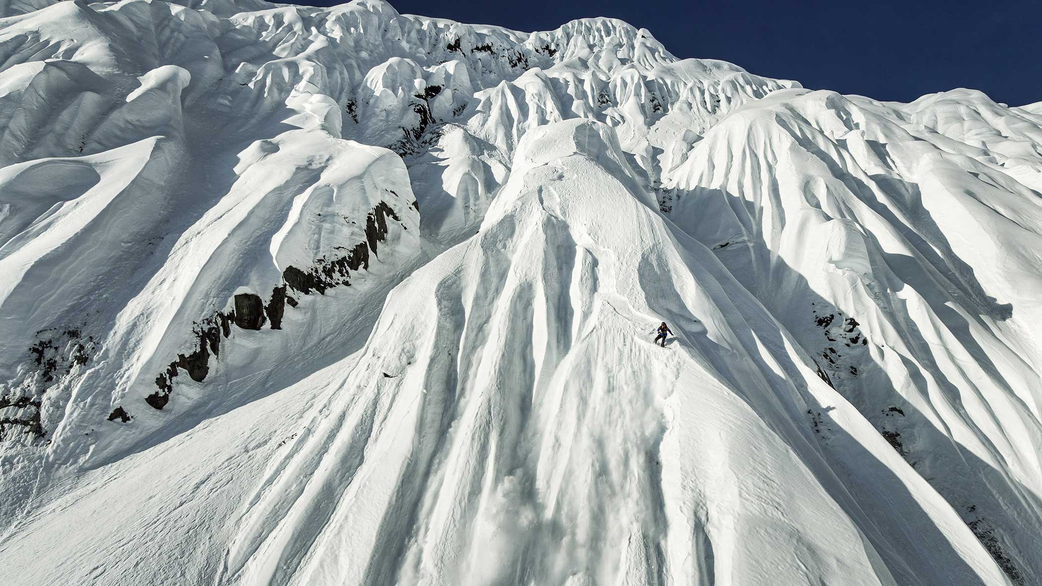 Snow-covered mountain with deep creases and ridges under a clear blue sky.