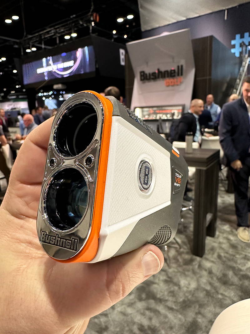 A hand holding and showing the front view of the Bushnell Tour V6 Shift rangefinder at the PGA Show