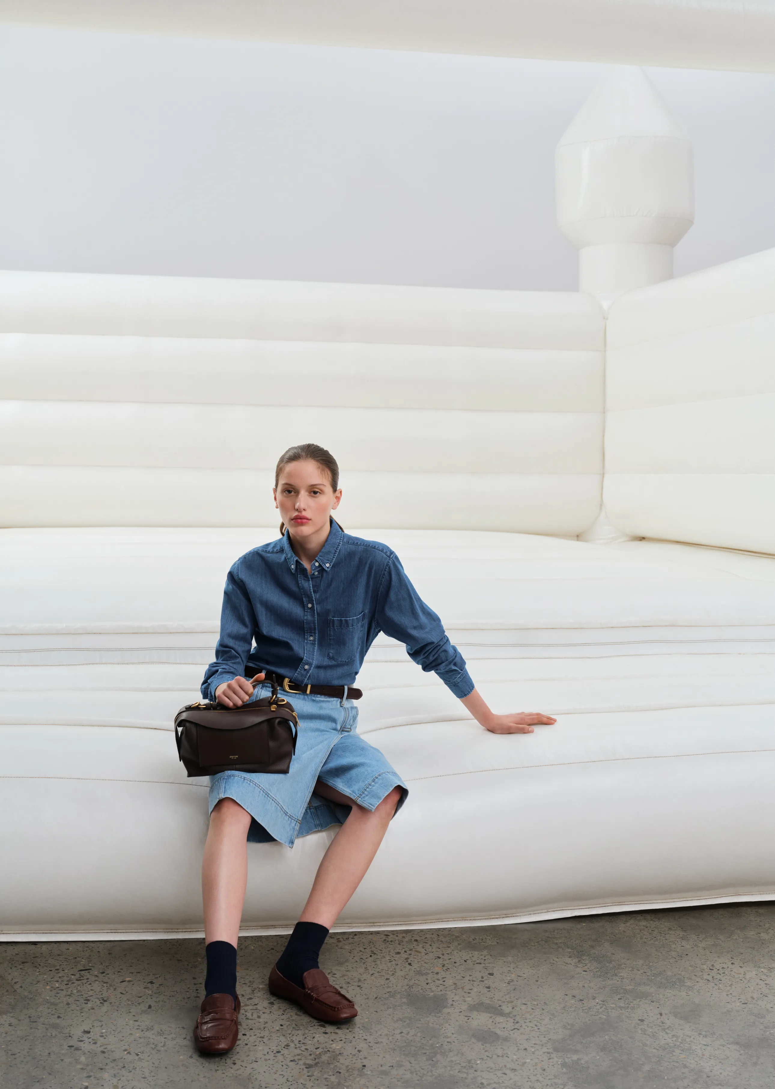 Person sitting on a large white inflatable structure, wearing denim and holding a bag.