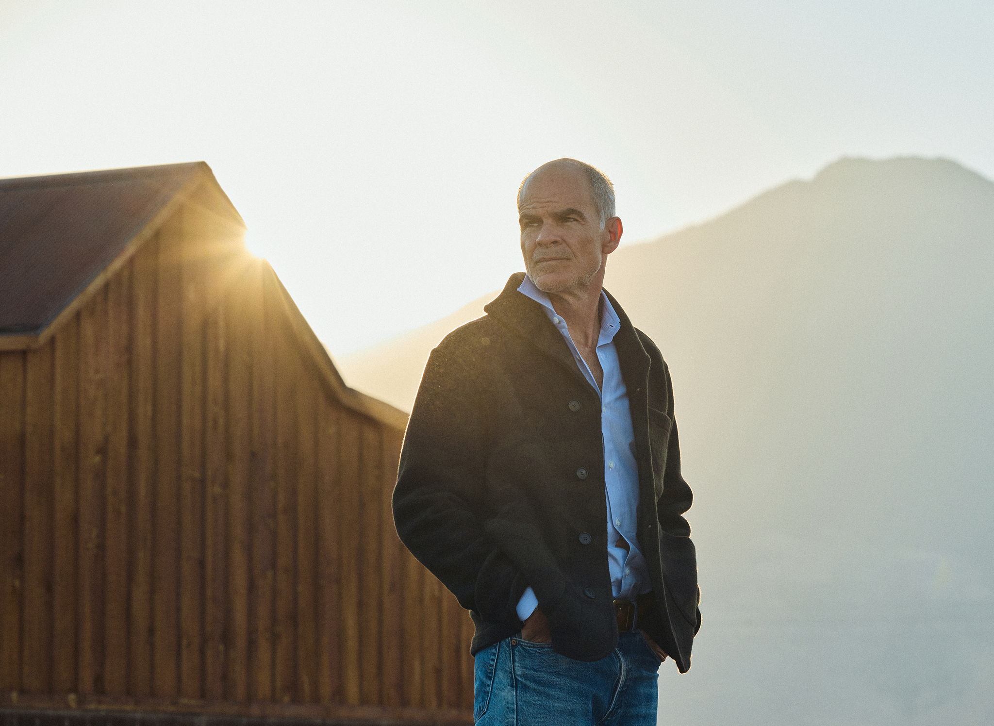 Micahel Kelly outside a barn in Pray Montana at sunrise wearing the Rivay Bridges Oxford Workshirt in Navy, the Hale Wool Cardigan in Olive Camouflage over the Corso Italian Dress Shirt in Classic Blue Micro Stripe and vintage pair of Levis
