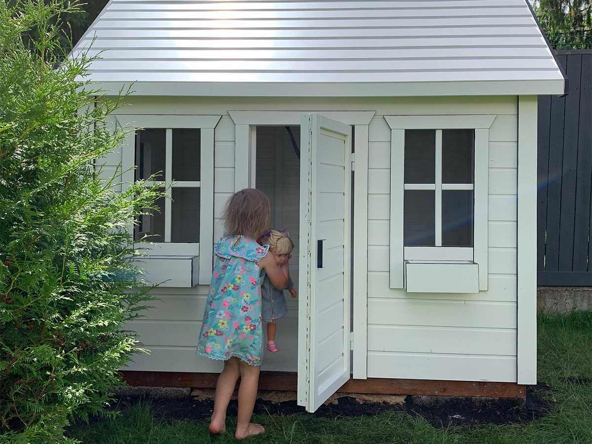 One kid looks inside the white outdoor playhouse Arctic Nario by WholeWoodPlayhouses