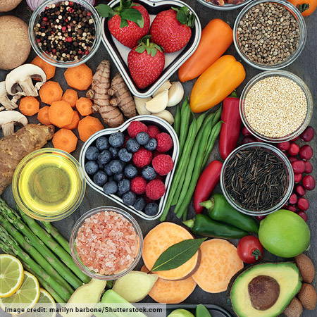 variety of fruits, vegetables, oils and grains on dark background and in stainless steel circular and heart shaped bowls