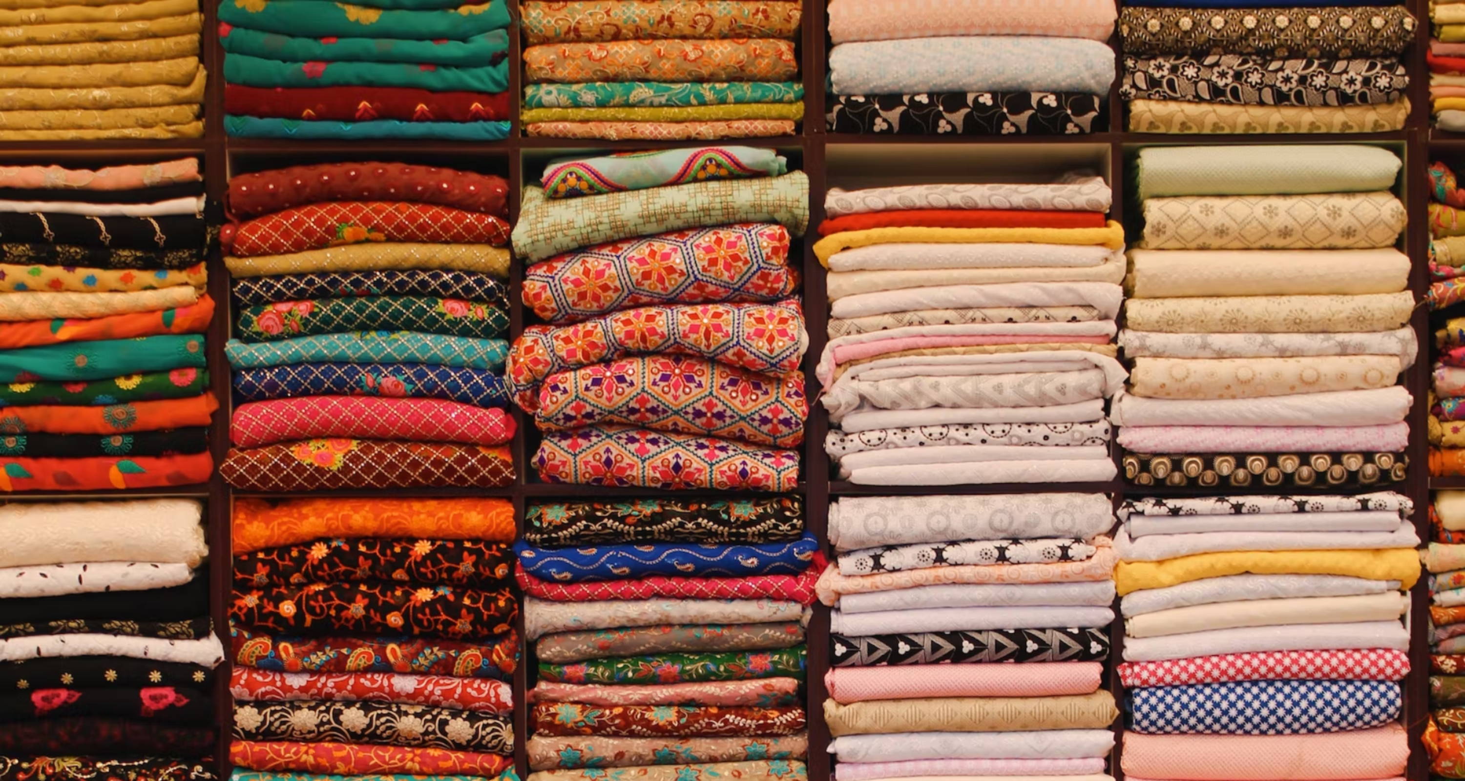 piles of neatly folded, colorful fabrics packed tightly in shelves 