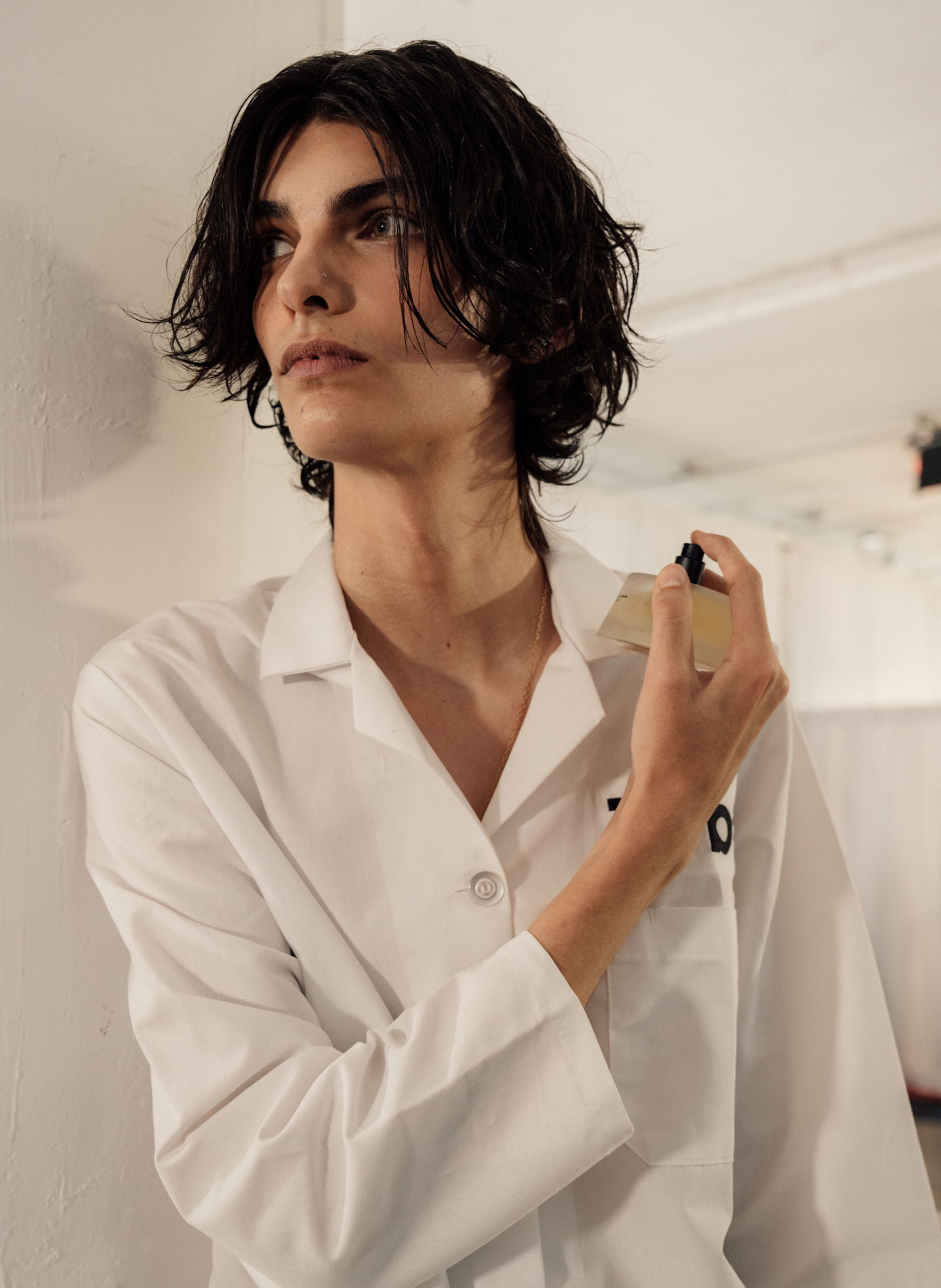 Person in a white shirt applying fragrance in a minimalistic setting.