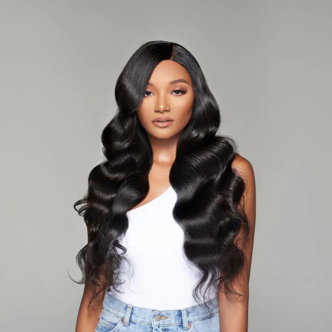 A woman with long, wavy hair extensions wearing a white top and jeans.