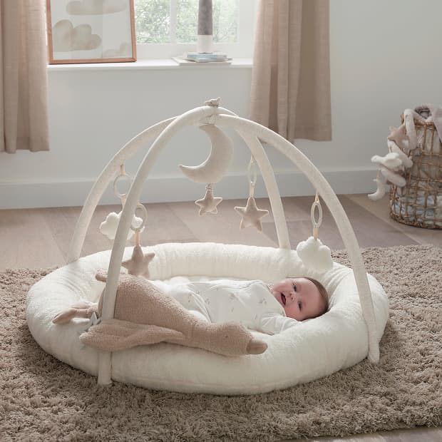 A baby lying on a play mat with hanging toys.