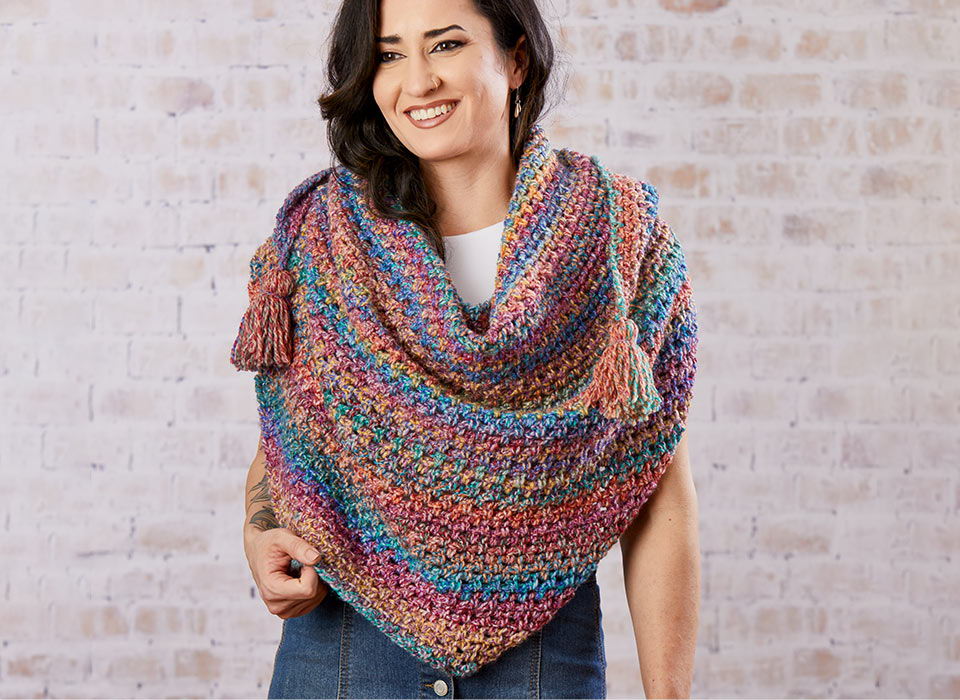 Smiling woman wearing a colorful knitted shawl against a textured background.
