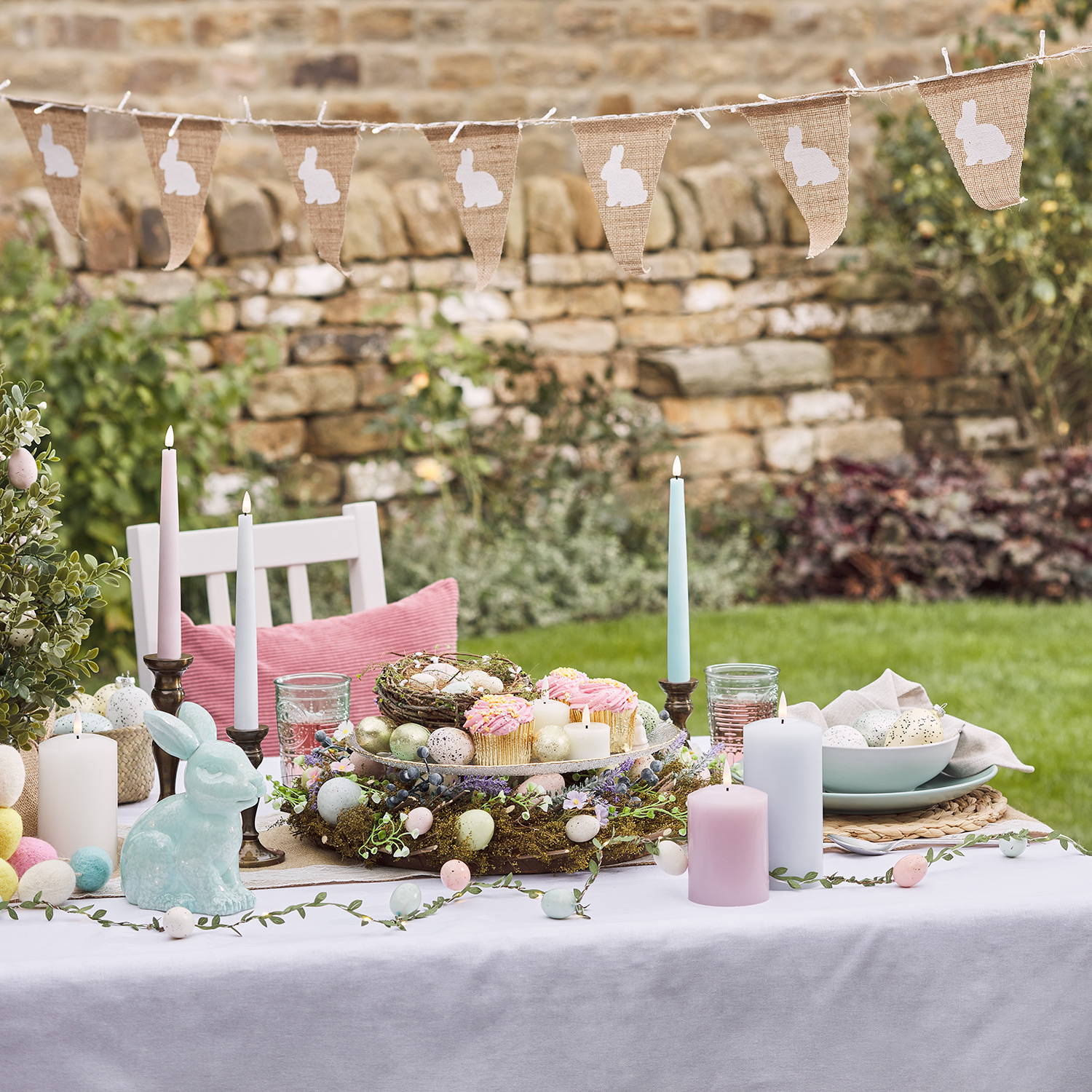 An outdoor Easter display for a party with wreaths, candles, bunting and a blue glass bunny.