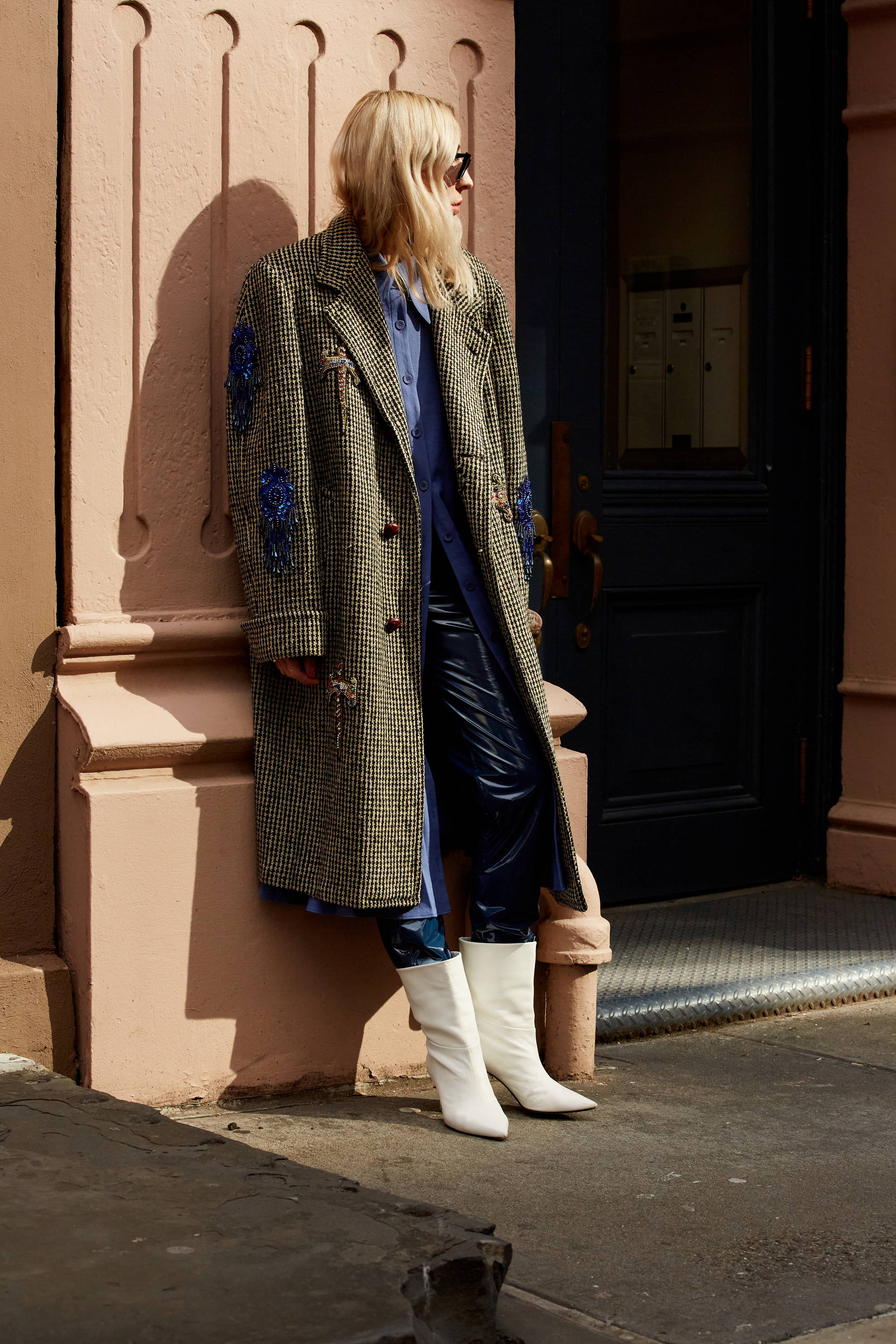 A person in a stylish coat and white boots leaning against a wall.