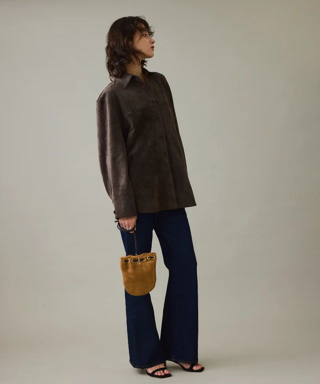 Model wearing a brown sweater and flared jeans, holding a handbag.