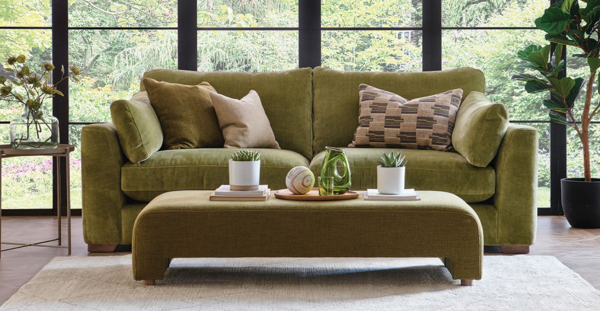 A comfy green fabric sofa with decorative pillows and a fabric coffee table.