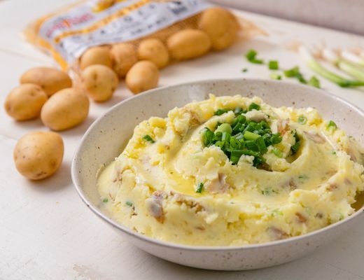 Bowl of mashed potatoes topped with green onions and nearby whole potatoes.