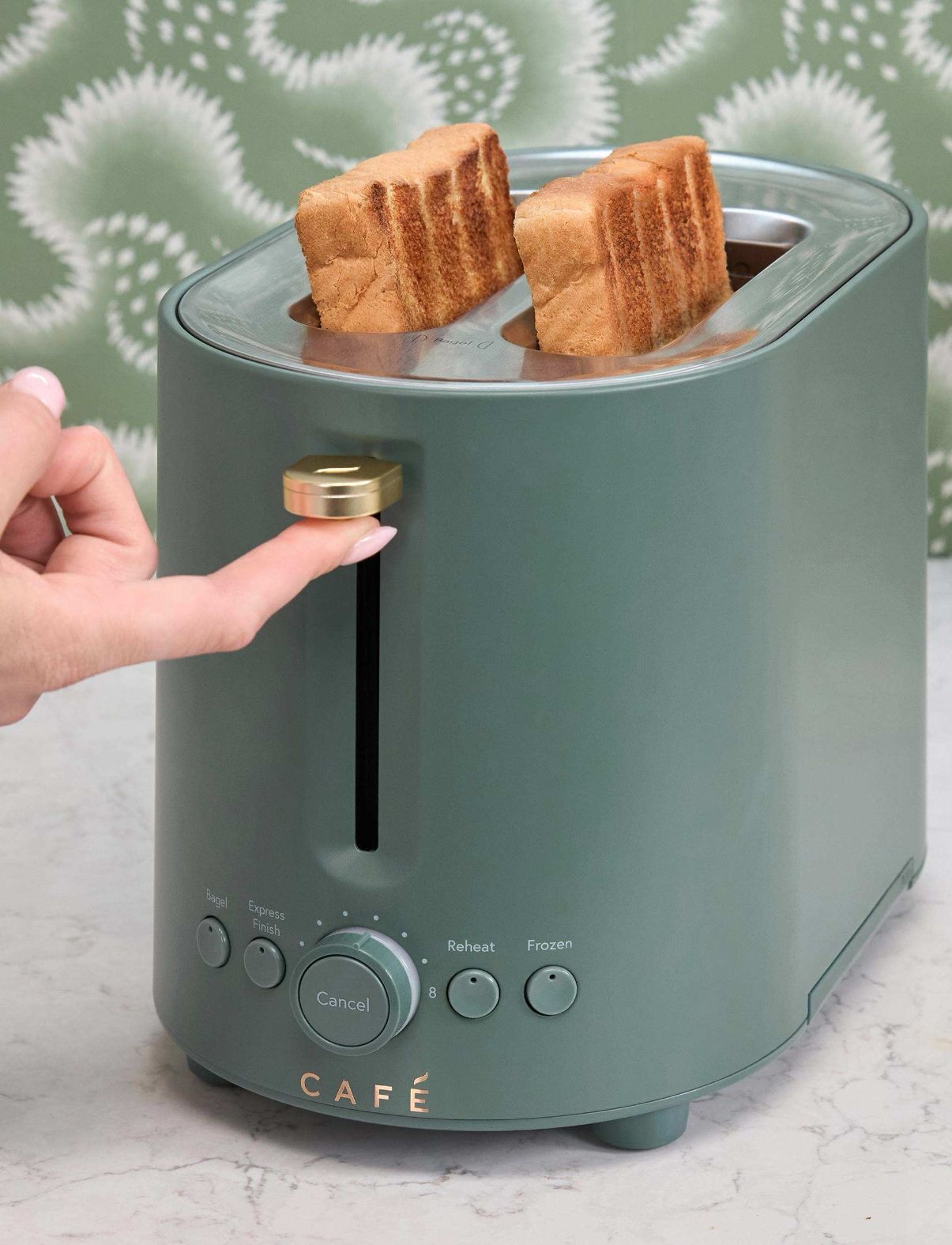 A hand adjusting a green toaster with two slices of bread inside.