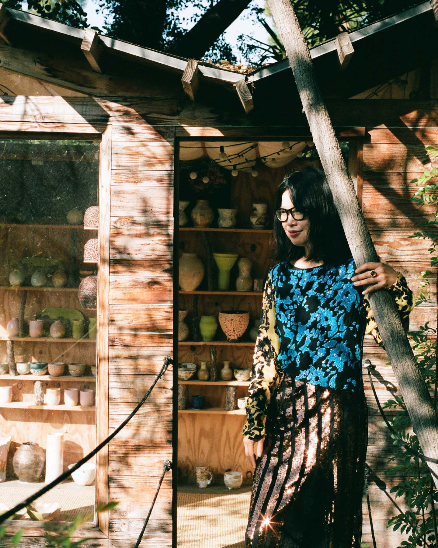 Raina Lee standing outside of her treehouse studio in a sequined dress.