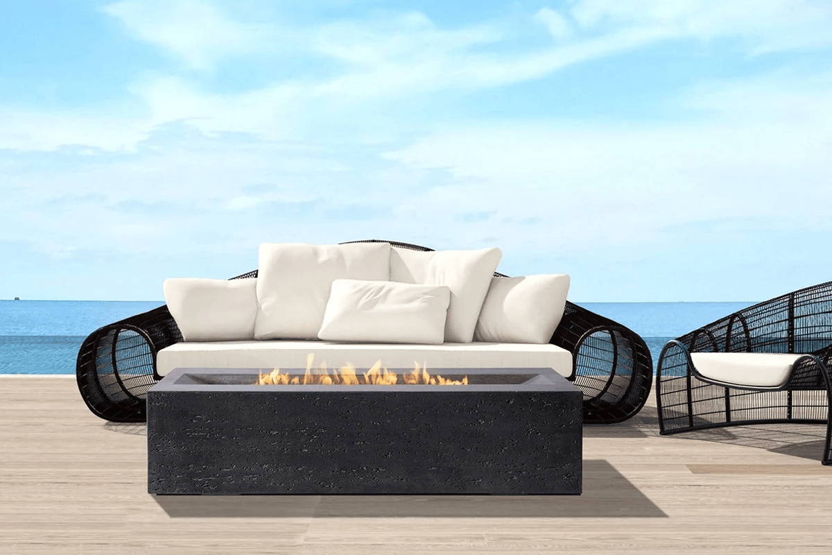 An inviting outdoor seating area on a wooden deck, featuring a black sofa, wicker chairs, and a captivating fire pit.