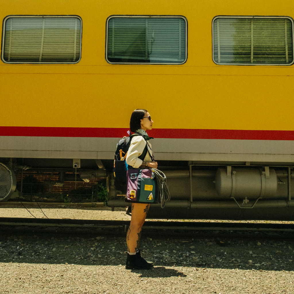 Person standing near a yellow train, wearing a backpack and casual outfit.