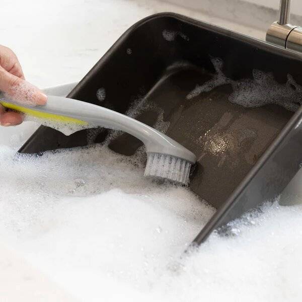 A baking tray is being scrubbed in soapy water with a cleaning brush.