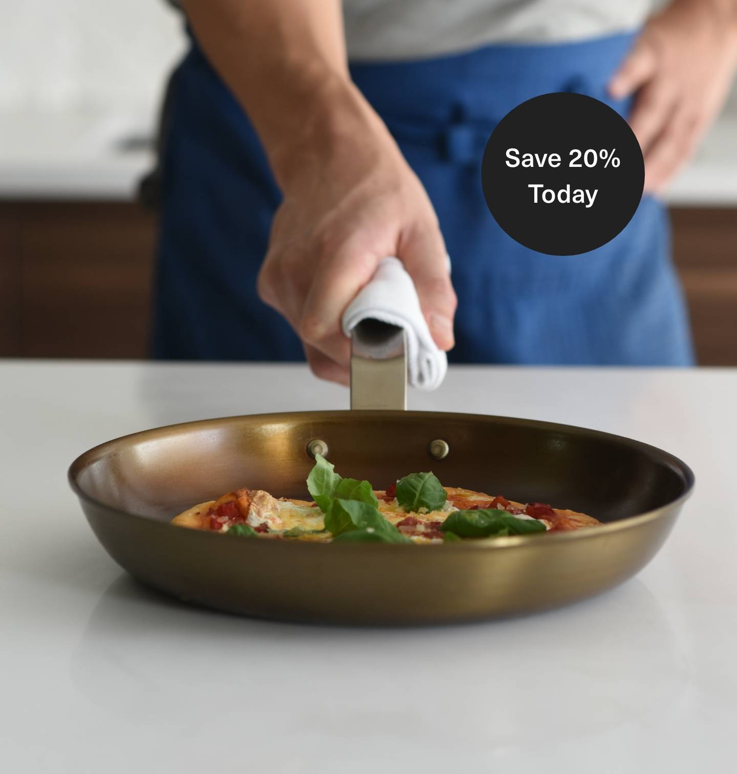 A chef holds a well-seasoned Misen Carbon Steel Pan with a kitchen towel around the handle. The pan contains a small pizza.