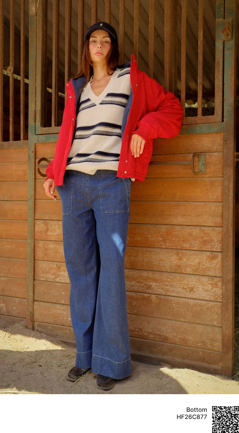 Person wearing a red jacket and striped shirt standing by a stable.
