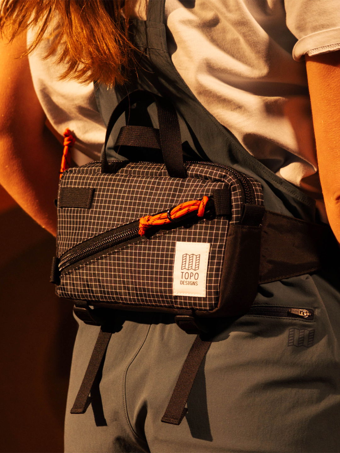 Person wearing a backpack with a checkered pattern and an orange pen attached.