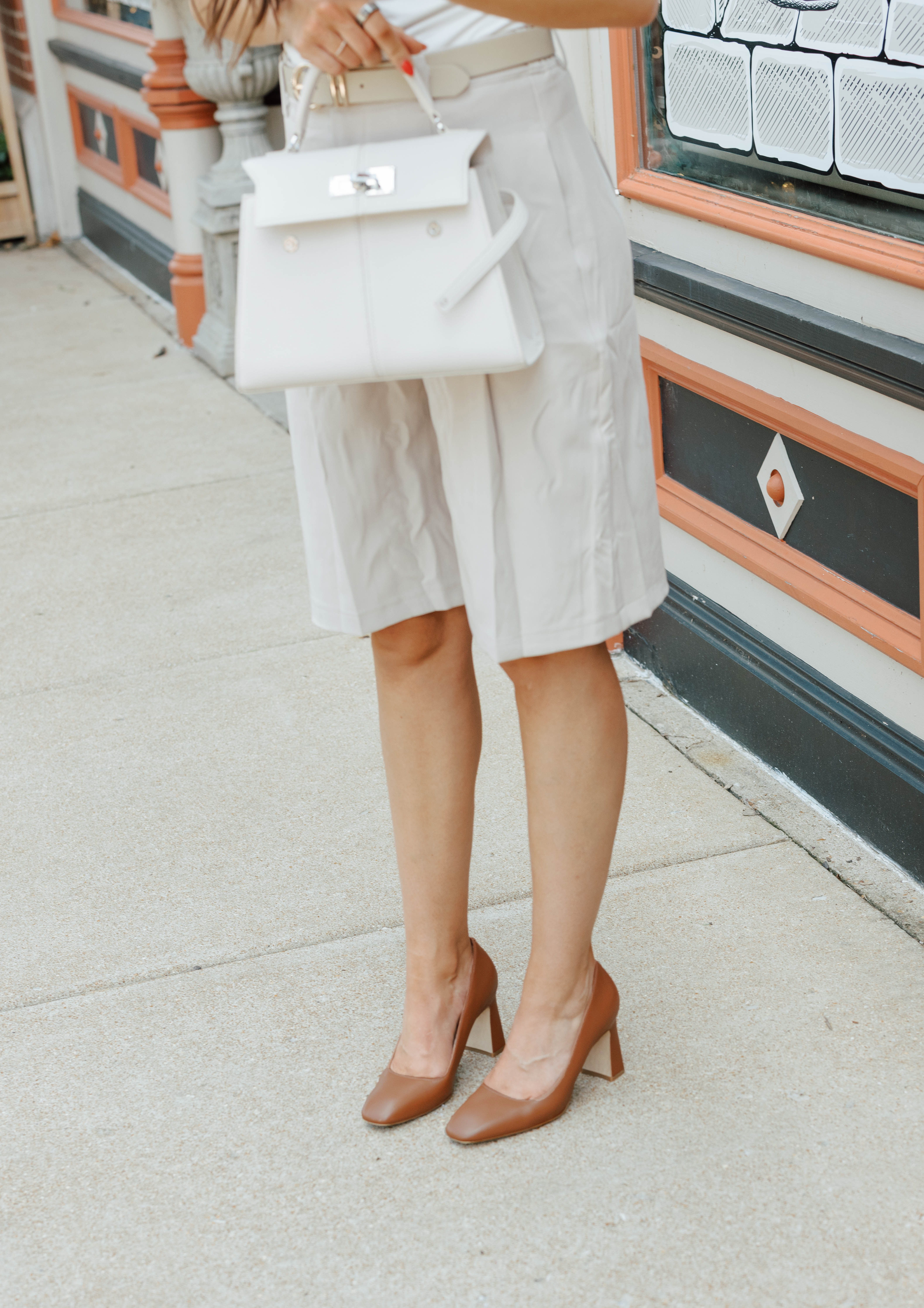 Person holding a handbag, wearing beige shorts and brown high heels.